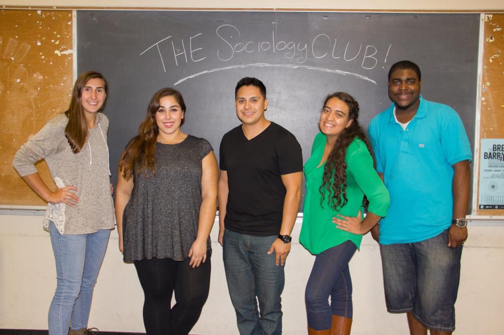Five sociology club members standing in front of a chalk board