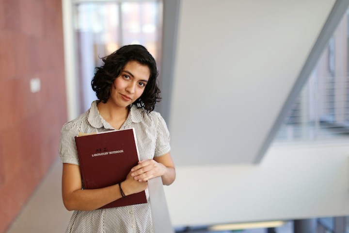 Student standing in a hallway, holding a folder, and smiling