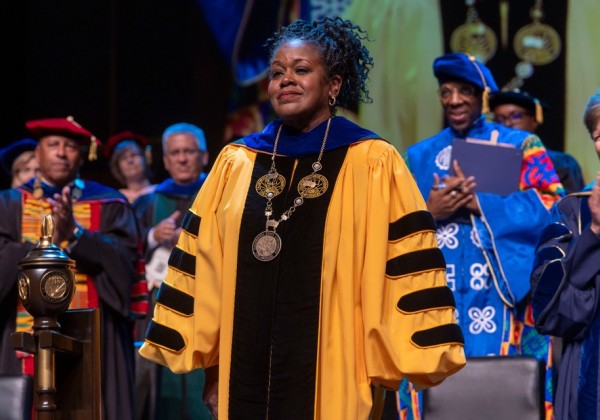 President of Cal State LA stands in gold academic regalia during the investiture ceremony, surrounded by applauding faculty in colorful gowns.
