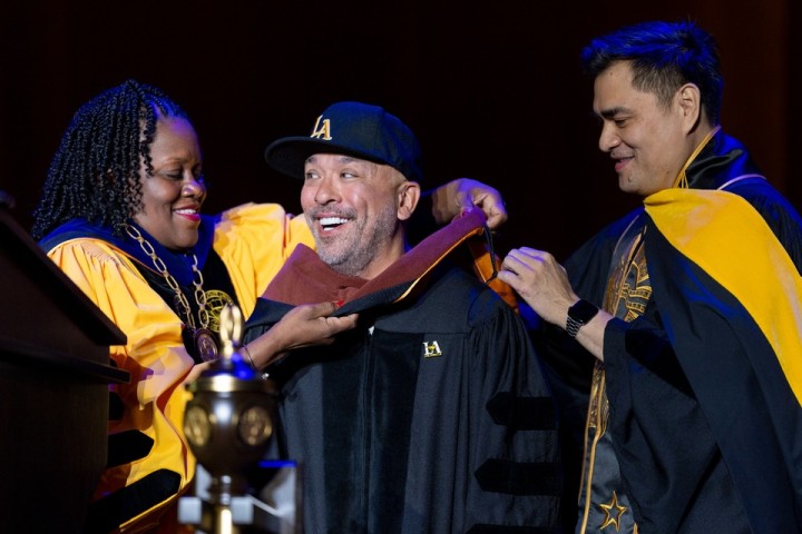 Comedian Jo Koy is hooded by President Berenecea Johnson Eanes during an honorary degree ceremony at Cal State LA’s 2025 commencement.