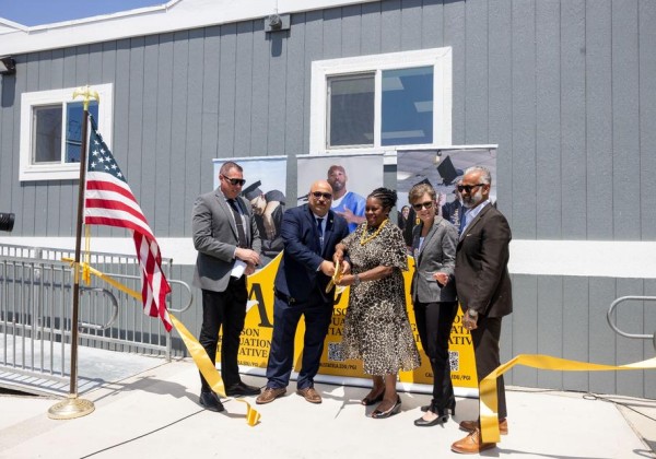 A group of officials and guests cut a yellow ribbon in front of banners for the Prison Graduation Initiative.